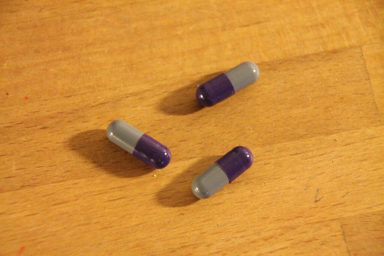 Photographie de trois gélules Medikinet 40 mg bicolores sur une surface en bois